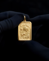 Gold pendant with a Grizzly bear design held by a gloved hand against a dark background
